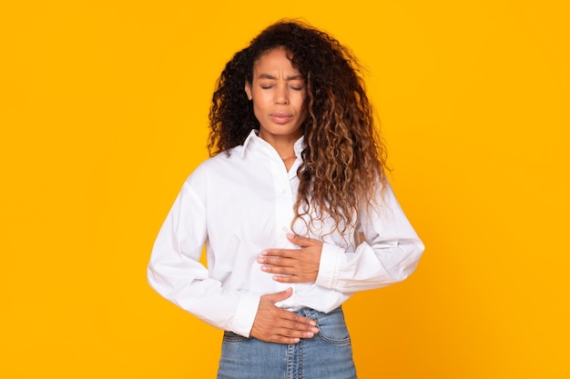 Jeune femme noire touchant l'estomac souffrant de maux d'estomac fond jaune