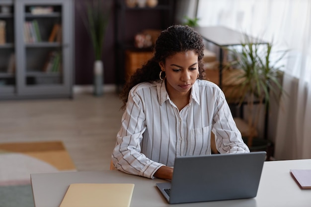 Jeune femme noire utilisant un ordinateur portable travaillant à domicile dans un cadre confortable