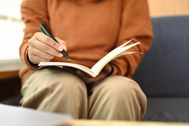 Une jeune femme non reconnaissable écrivant des notes dans son agenda personnel ou planifiant sa journée de travail.