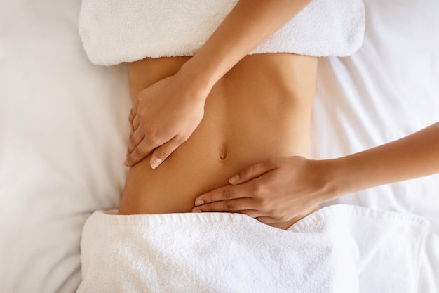 Une jeune femme non reconnaissable recevant un massage pour la région abdominale à l'intérieur