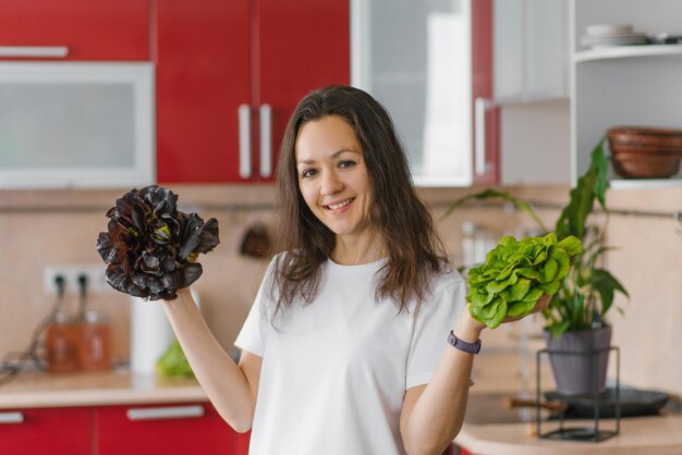 Jeune femme nutritionniste végétarienne heureuse tient deux types de salade dans ses mains des aliments biologiques naturels des aliments sains à la maison