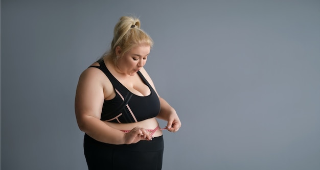 Jeune femme obèse dodue mesurant la taille avec un ruban à mesurer