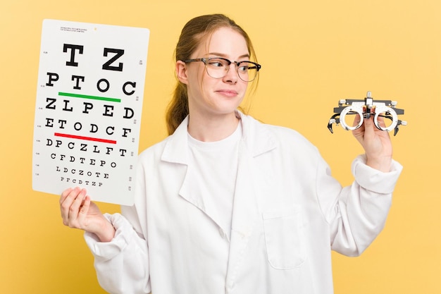 Jeune femme oculiste caucasienne faisant un examen de la vue isolé sur fond jaune