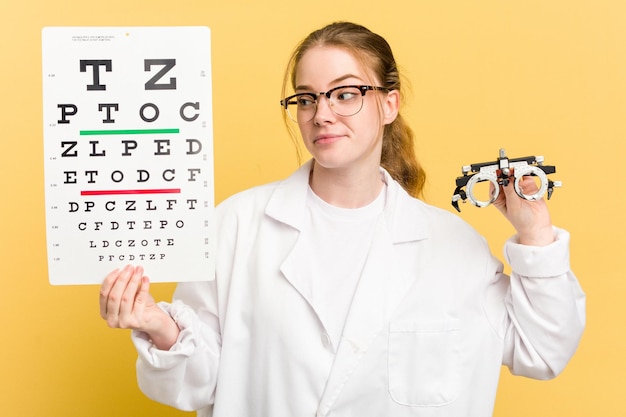 Jeune femme oculiste caucasienne faisant un examen de la vue isolé sur fond jaune