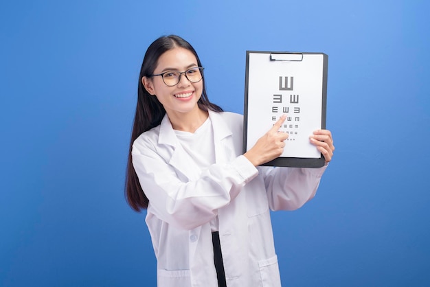 Une jeune femme ophtalmologiste avec des lunettes tenant un tableau des yeux sur fond bleu studio, concept de soins de santé