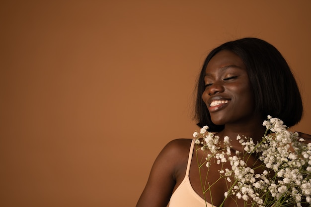 Une jeune femme optimiste aux yeux fermés et à l'expression satisfaite porte de belles fleurs blanches près d'elle-même