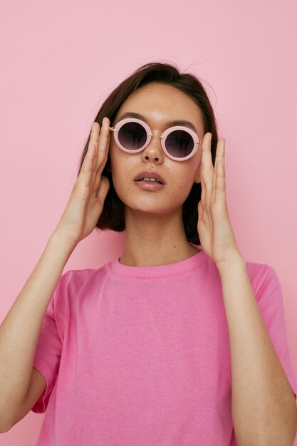 Jeune femme optimiste en lunettes de soleil un t-shirt rose Style de vie inchangé