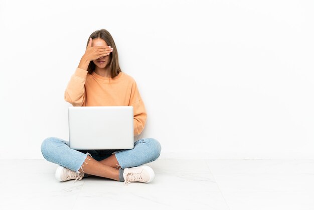 Jeune femme avec un ordinateur portable assis sur le sol couvrant les yeux à la main. Je ne veux pas voir quelque chose