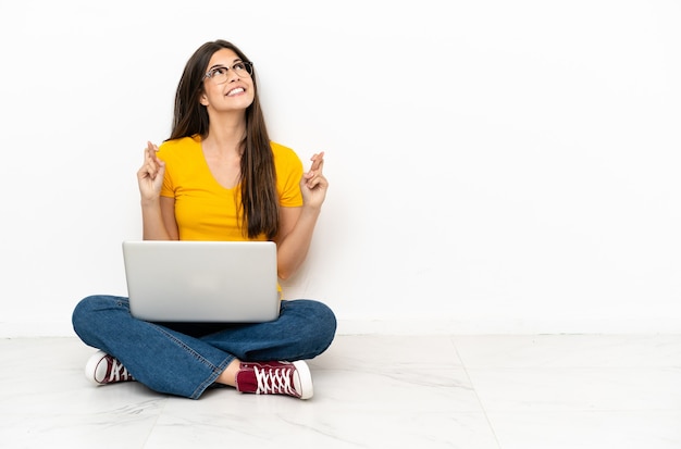 Jeune femme avec un ordinateur portable assis sur le sol avec les doigts qui se croisent