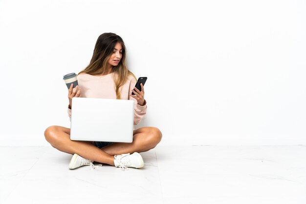Jeune femme avec un ordinateur portable assis sur le sol isolé