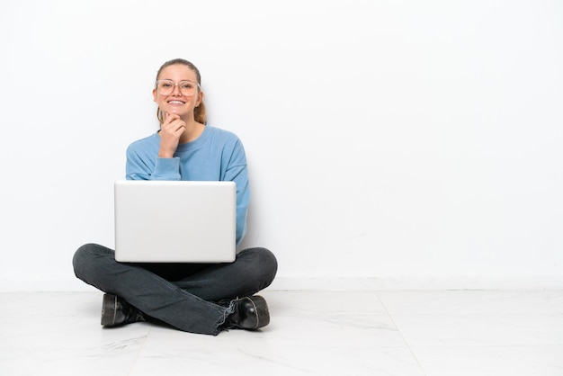 Jeune femme avec un ordinateur portable assis sur le sol avec des lunettes et souriant