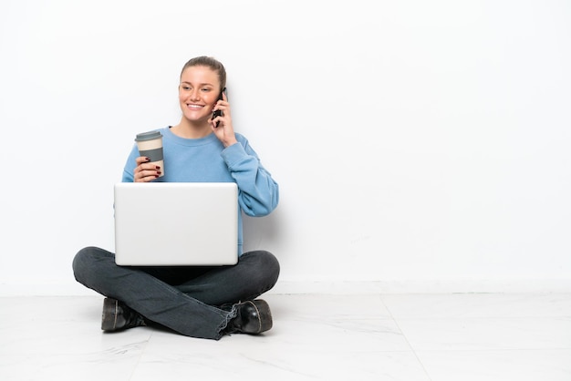 Jeune femme avec un ordinateur portable assis sur le sol tenant du café à emporter et un mobile