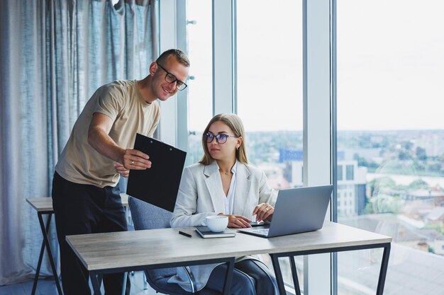 Une jeune femme à un ordinateur portable dans des verres est assise à une table ayant une réunion d'affaires d'entreprise avec des collègues dans un concept de carrière d'affaires de bureau moderne Mise au point sélective de l'espace libre