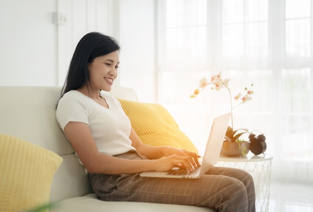 Jeune femme avec un ordinateur portable moderne assis sur un canapé à la maison