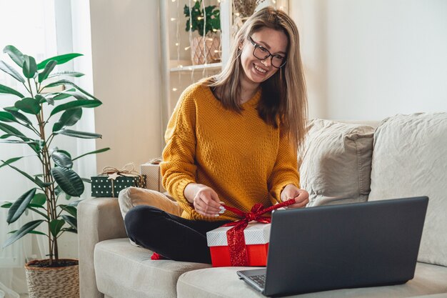 Jeune femme avec ordinateur portable ouvrant un cadeau de Noël