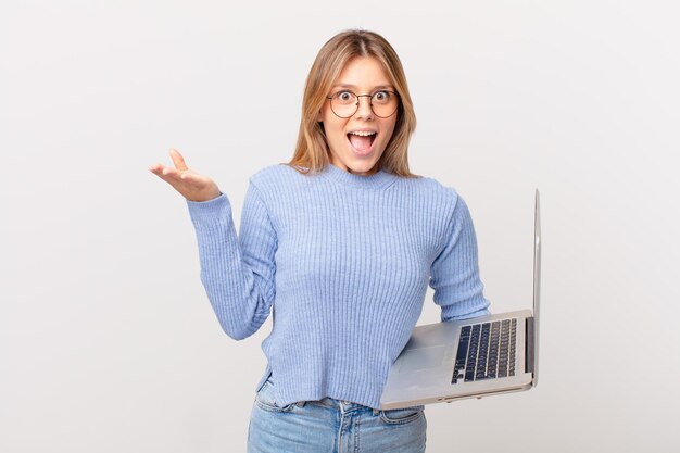 Jeune femme avec un ordinateur portable se sentant extrêmement choquée et surprise