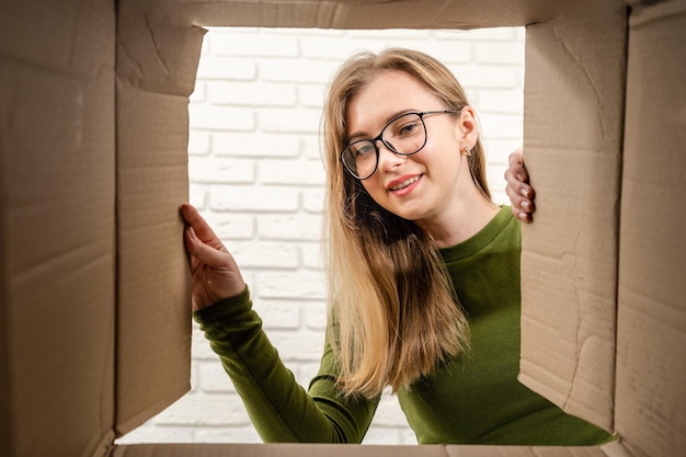 Photo jeune femme ouvrant une boîte en carton et regardant à l'intérieur