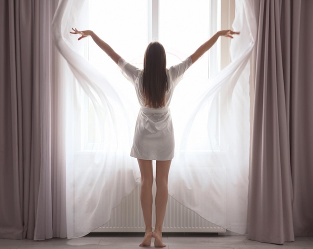 Jeune femme ouvrant des rideaux à la maison