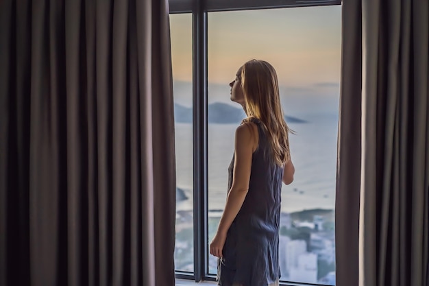 La jeune femme ouvre les rideaux sur une fenêtre de vue de mer