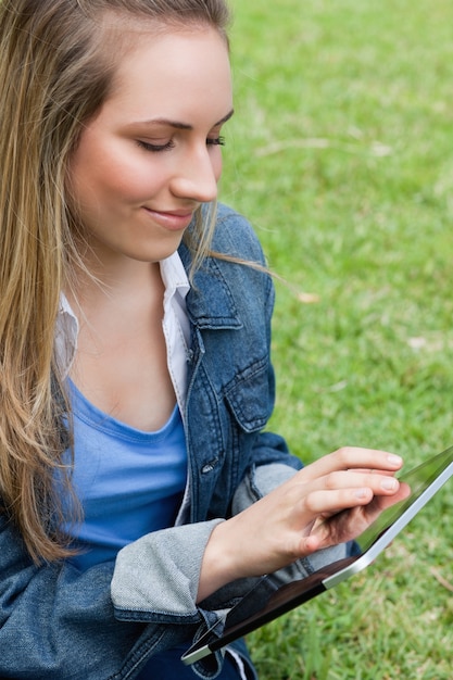 Jeune femme paisible à l&#39;aide de son tablet pc assis sur l&#39;herbe