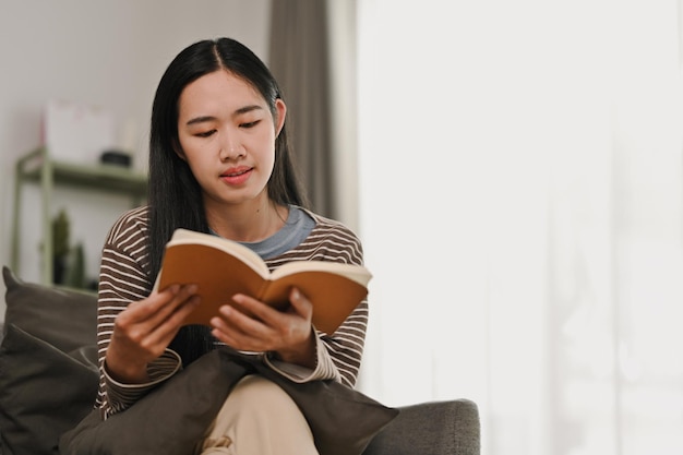 Une jeune femme paisible qui lit un livre et se détend sur le canapé dans un salon confortable.