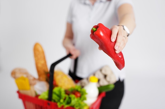 Jeune femme avec panier rempli de produits choisissant des légumes sur le marché