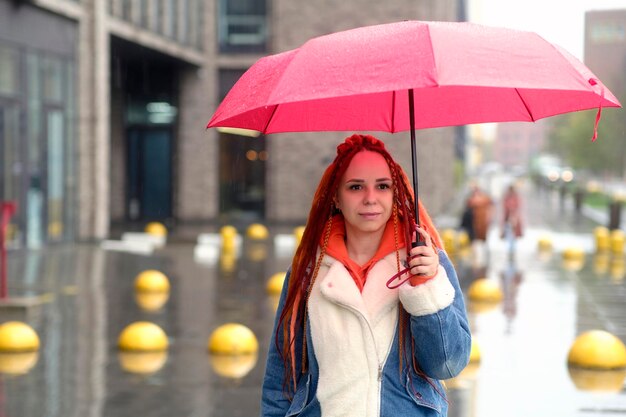 Jeune femme avec un parapluie dans la rue Jeune femme positive dans des vêtements chauds souriant debout dans la rue de la ville