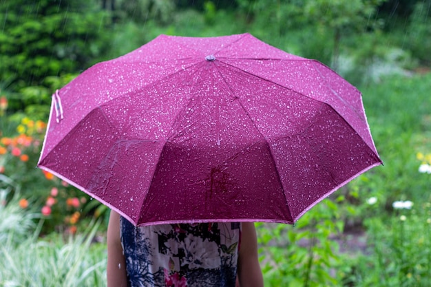 Une jeune femme avec un parapluie violet dans le parc un jour d'été pluvieux vue de l'arrière