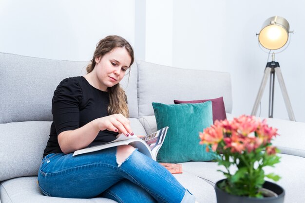 Jeune femme parcourant le magazine de décoration dans son salon. Réformes, style de vie et intérieurs.