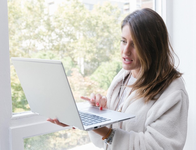 Jeune femme parcourant un ordinateur portable près de la fenêtre le matin