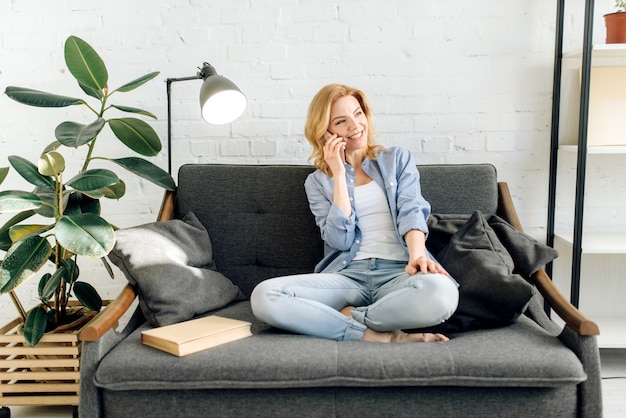 Jeune femme parlant par téléphone mobile sur un canapé noir confortable