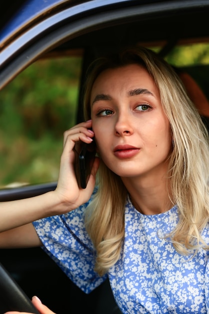 Jeune femme parlant sur un téléphone portable alors qu'elle était assise dans la voiture sur le siège du conducteur. Étudiante blonde attirante