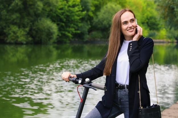 Une jeune femme parle au téléphone à côté d'un scooter électrique dans le parc