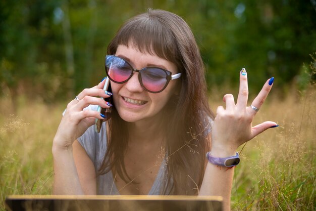 Une jeune femme parle avec émotion au téléphone sur la pelouse par une journée ensoleillée. émotion heureuse sur le visage.