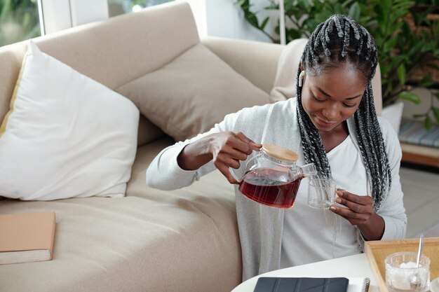 Jeune femme passant le week-end à la maison, elle est assise par terre et se verse une tasse de thé