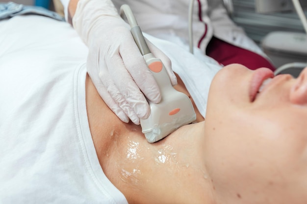 Jeune femme patiente lors de l'échographie d'une thyroïde allongée sur le canapé