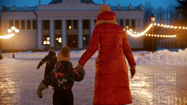 Une jeune femme patinant sur une patinoire publique avec ses enfants tenant sa fille à la main