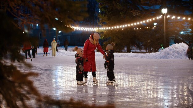 Une jeune femme patinant sur la patinoire avec ses petits enfants