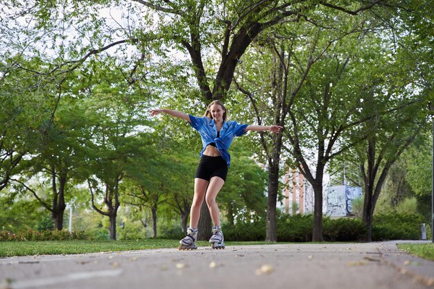Jeune femme patinant sur des patins à roues alignées dans le parc à bras ouverts