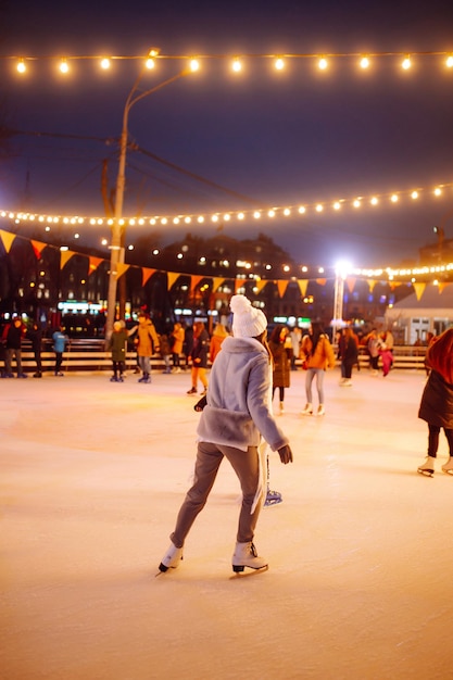 Jeune femme patiner sur une patinoire dans une foire de Noël festive le soir. Lumières autour.