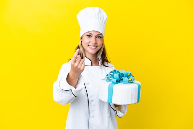 Jeune femme pâtissière russe avec un gros gâteau isolé sur fond jaune faisant un geste à venir