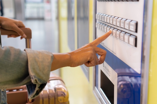 Jeune femme payant au distributeur de billets dans une gare