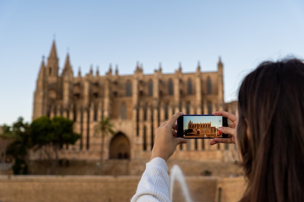 Photo jeune femme à la peau claire prenant une photo de la cathédrale de palma de majorque avec son téléphone pendant ses vacances.