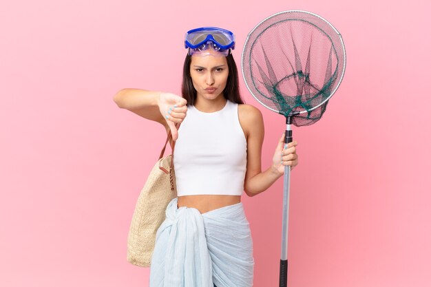 Jeune femme pêcheuse se sentant croisée, montrant les pouces vers le bas et les lunettes de plongée