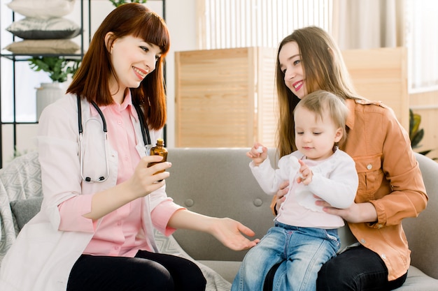 Jeune Femme Pédiatre Prescrit Et Donne Un Médicament à Une Petite Fille Malade, Assise Avec Sa Mère