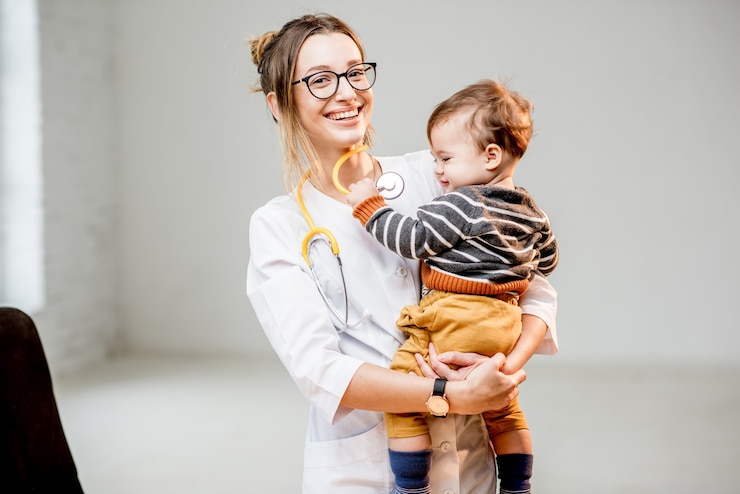 Photo jeune femme pédiatre en robe médicale debout avec bébé garçon à l'intérieur du bureau blanc