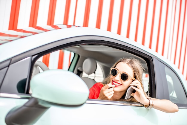 Jeune femme peignant des lèvres alors qu'elle était assise à la voiture sur le fond de mur rayé pendant les vacances d'été