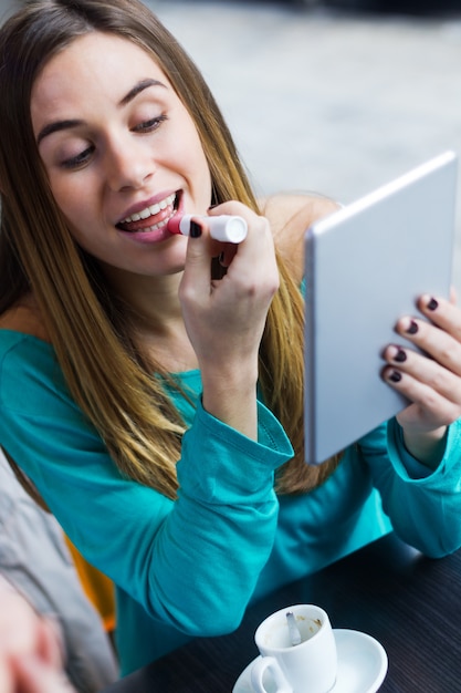 jeune femme peignant ses lèvres avec une tablette numérique dans un café