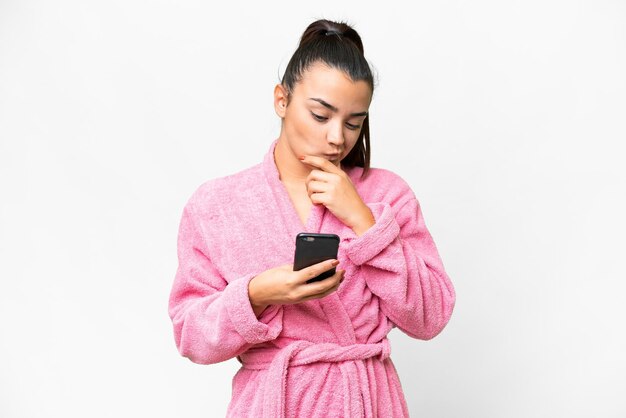 Une jeune femme en peignoir sur un fond blanc isolé pense et envoie un message