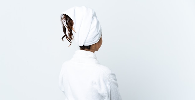 Jeune femme en peignoir sur fond blanc isolé en position arrière et regardant en arrière
